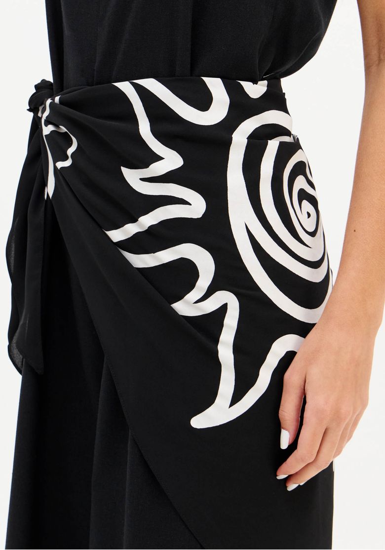 Lenço estampado preto e branco amarrado na cintura do macacão, detalhe da amarração e estampa gráfica