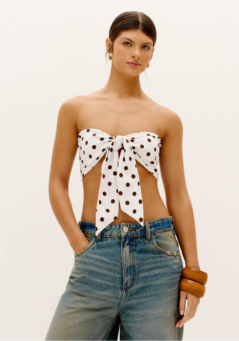 Modelo vestindo top faixa estampado com poá e calça jeans, vista frontal.
