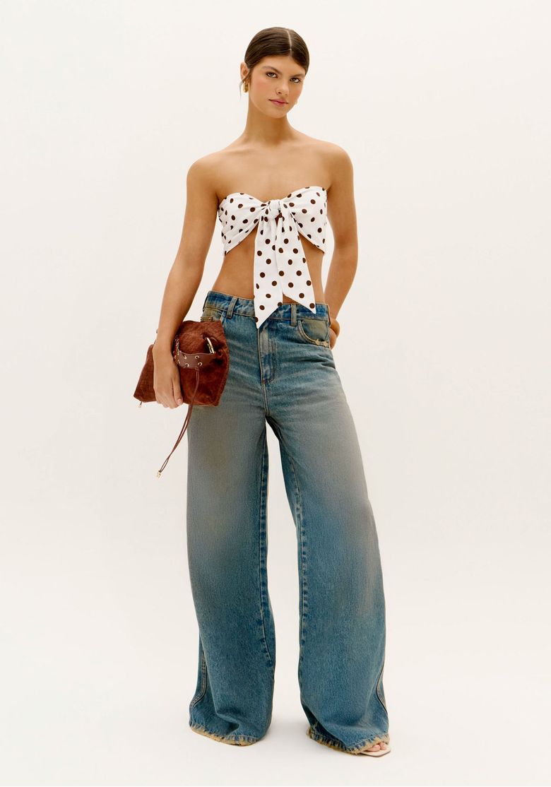 Modelo vestindo top faixa estampado com poá e calça jeans, segurando bolsa.
