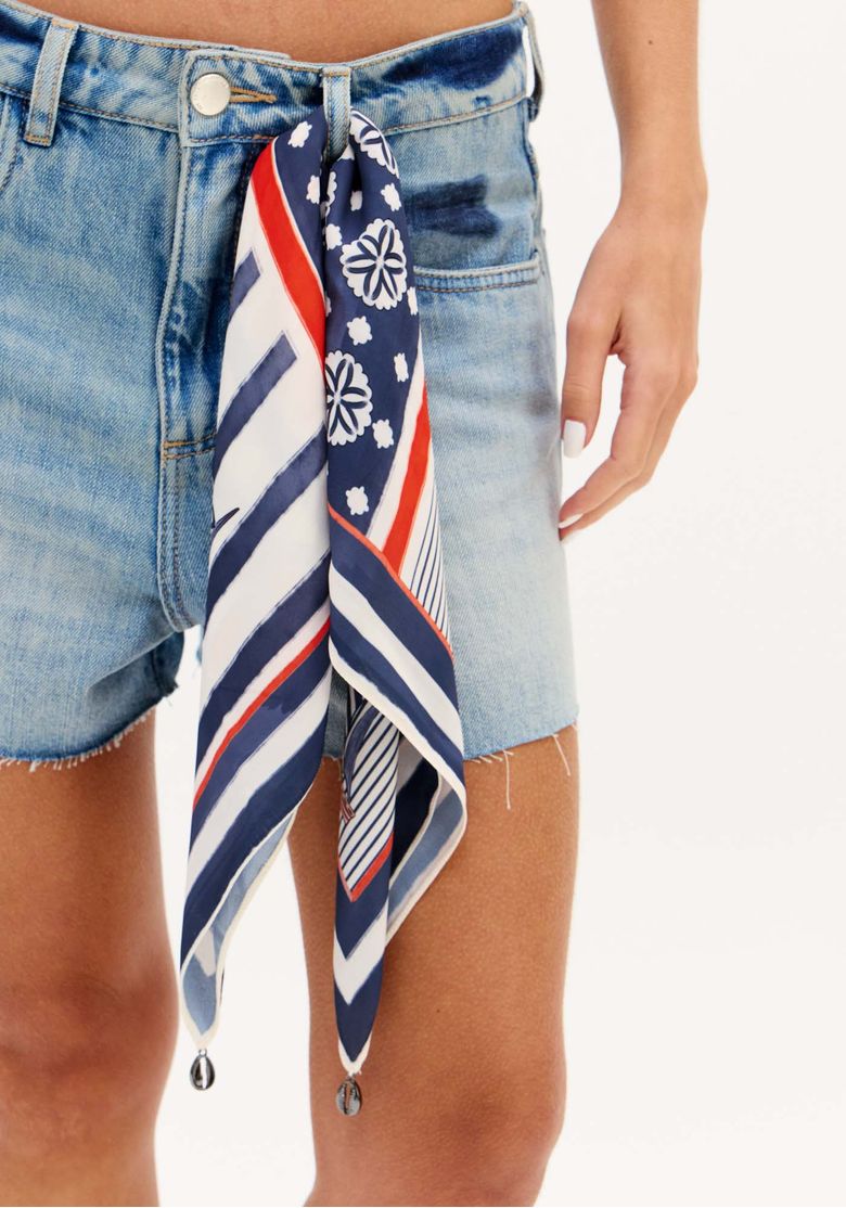 Detalhe frontal do short jeans relaxed azul claro com botão, passantes no cós e lenço estampado em azul, branco e vermelho