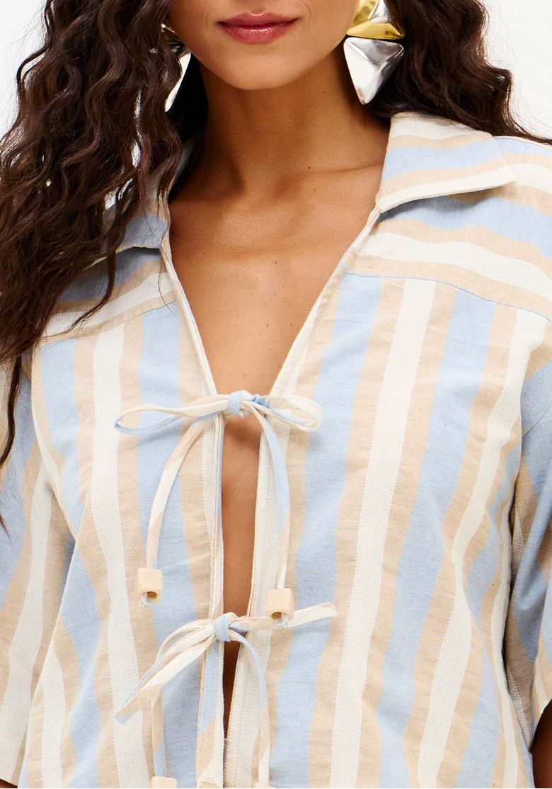 Vista frontal da camisa alongada feminina com listras verticais, mangas amplas e fechamento por laços frontais