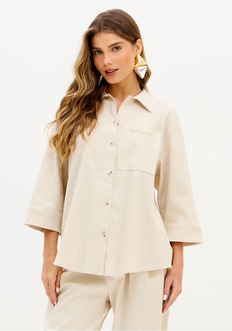 Vista frontal da camisa feminina oversized bege com manga 7/8, modelagem ampla e barra arredondada
