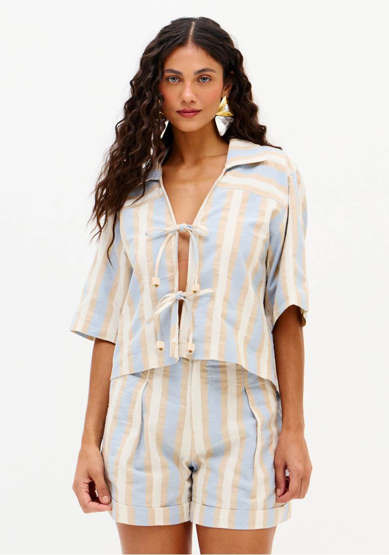 Close da camisa feminina listrada alongada com mangas curtas, gola aberta e amarração frontal em tons de azul claro e bege