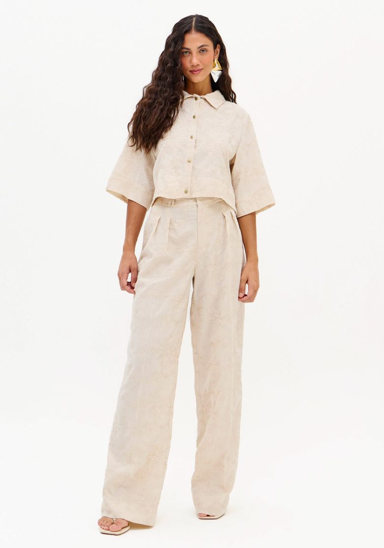 Modelo vestindo calça full length bege cintura alta com bordado em relevo e top cropped, vista frontal em estúdio com fundo branco