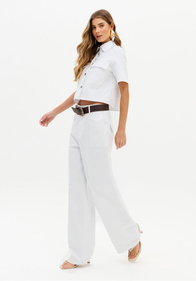 Modelo caminhando com calça reta branca e top branco, vista lateral.