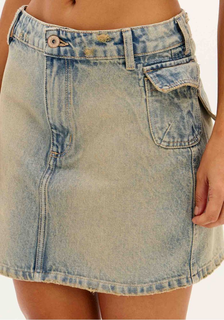 Close-up frontal da saia jeans cargo mostrando cós com botão, costura central e barra com leve acabamento desfiado