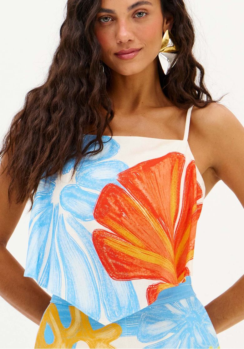 Close da blusa lenço mostrando estampa maxi floral em laranja e azul sobre base branca, detalhe da barra assimétrica e alça fina