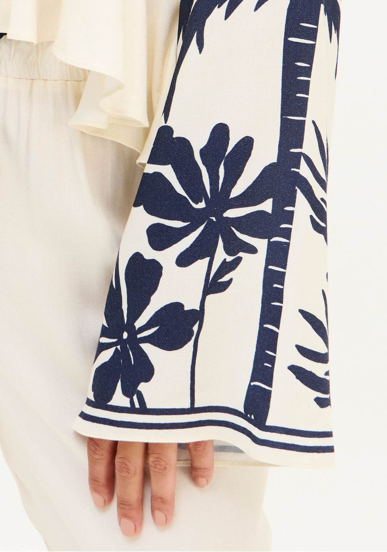 Detalhe da manga longa ampla da blusa com estampa tropical azul sobre fundo branco e acabamento fluido na barra