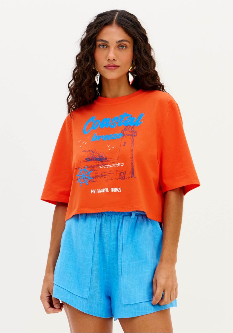 Modelo vestindo t-shirt oversized cropped vermelha com estampa frontal, combinada com shorts azul.