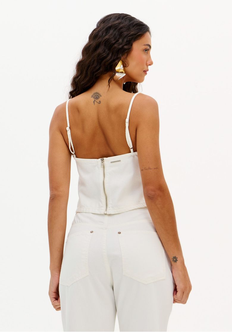 Modelo usando a blusa com calça branca, mostrando o look completo.