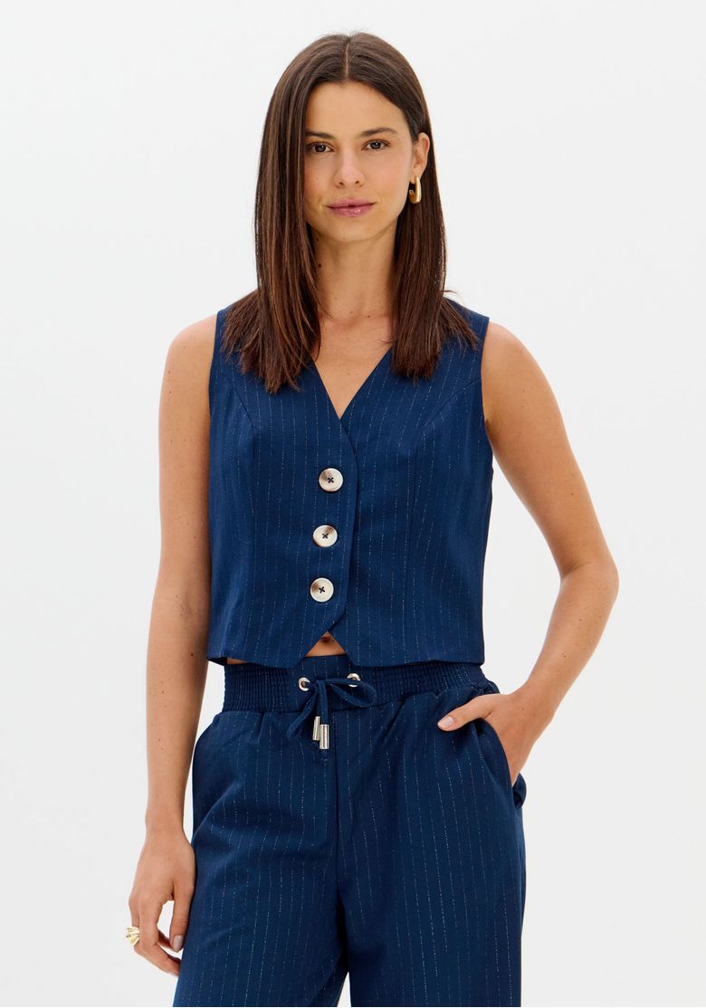 Modelo em estúdio veste colete curto risca de giz azul, vista frontal com decote em V e botões maxi, look coordenado com calça combinando
