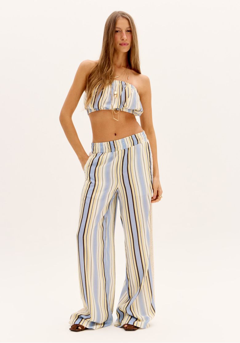 Modelo em pé vista frontal usando calça wide leg listrada azul e creme em viscose com linho, cós elástico e caimento fluido, combinada com top faixa cropped