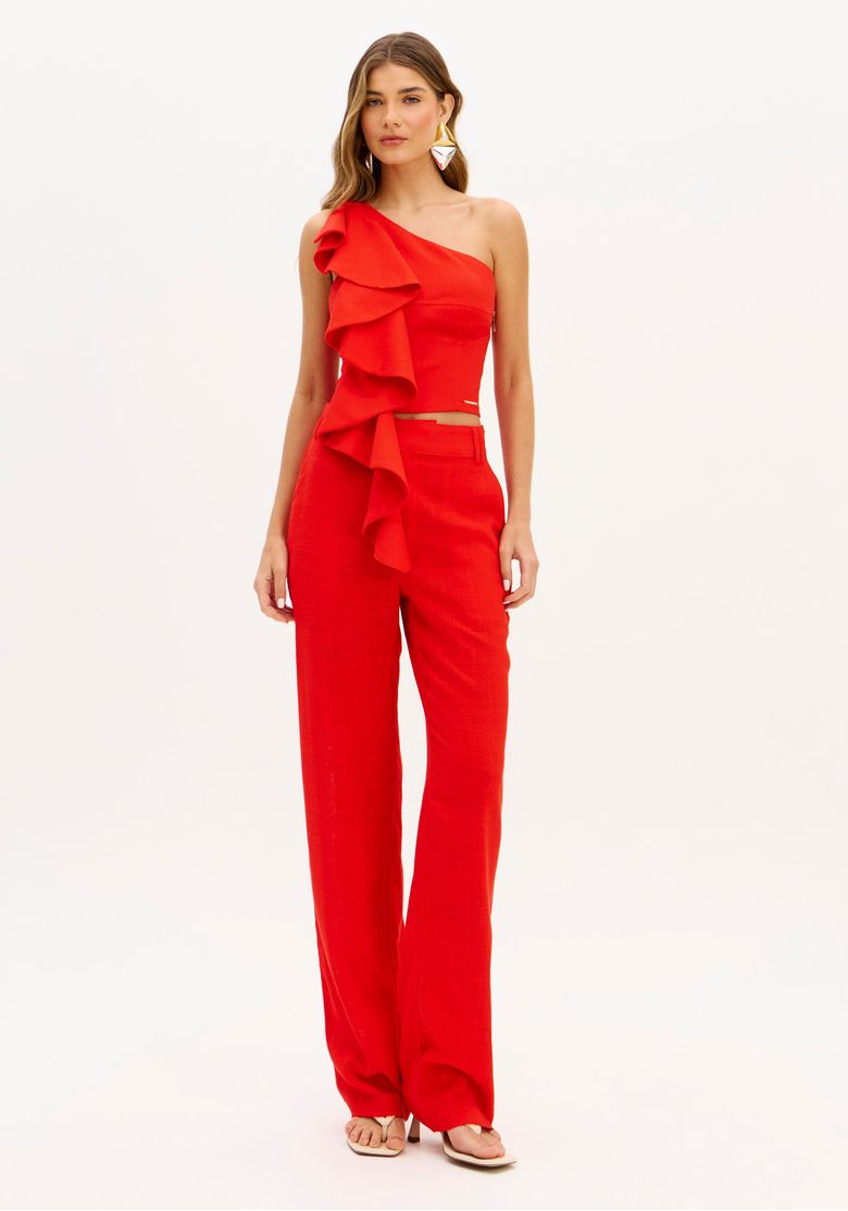 Modelo vestindo calça reta de linho vermelho e top com babado de ombro único, vista frontal do look completo.