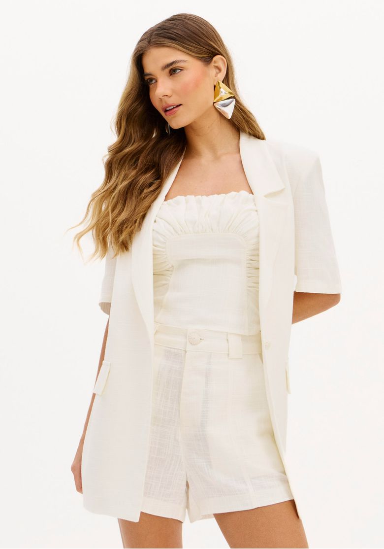 Modelo usando blazer feminino alongado com manga curta, em um look completo.