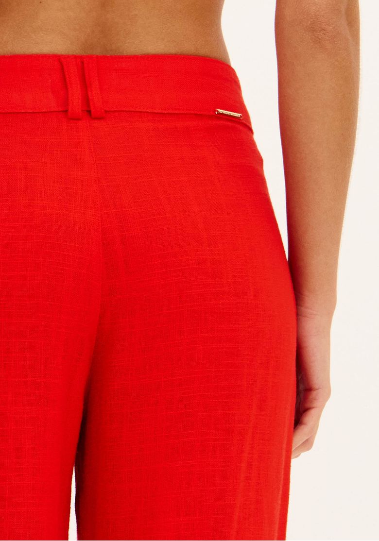 Detalhe da parte traseira do cós da calça vermelha com passantes e bolso embutido discreto com componente metálico.