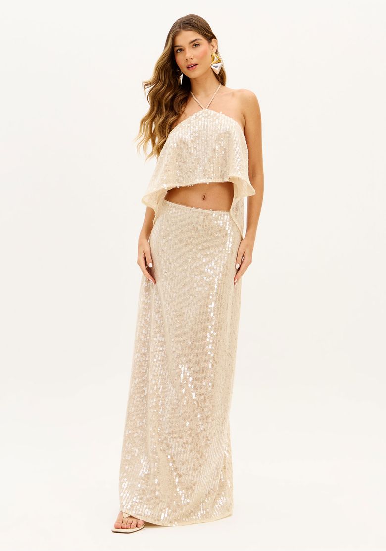 Modelo em pé usando saia midi evasê em paetês bege com top halter cropped combinando; cintura alta e caimento fluido, look festa noturna