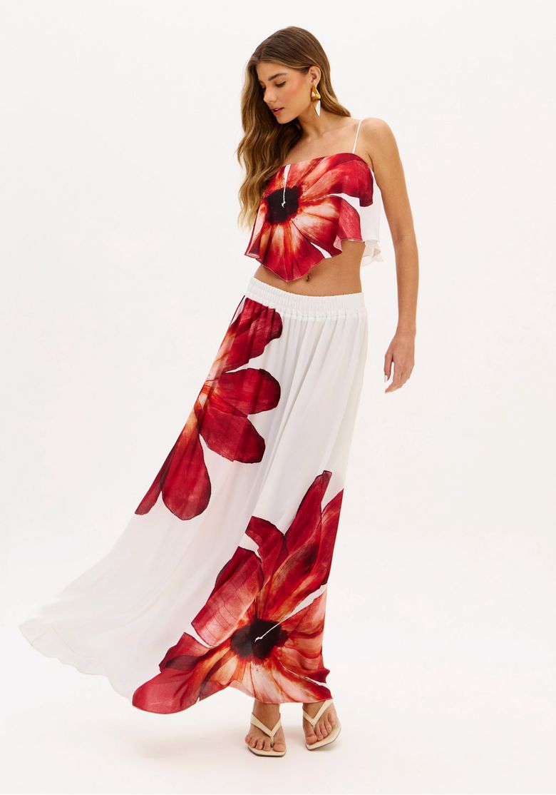 Modelo usando saia longa estampada com flores vermelhas e top combinando, em fundo branco.