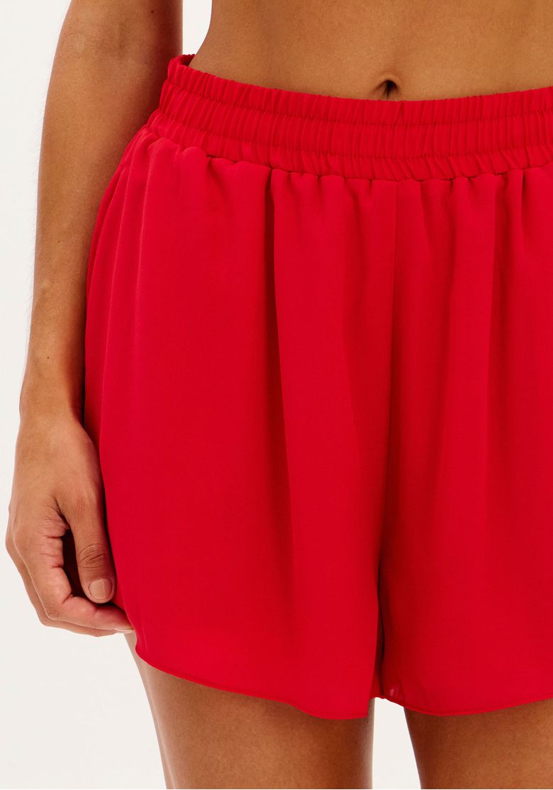 Detalhe do short evasê vermelho com cós de elástico.