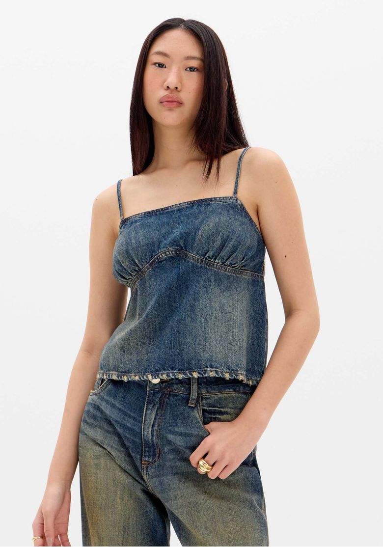 Blusa jeans feminina com alças finas e barra desfiada, vista frontal.