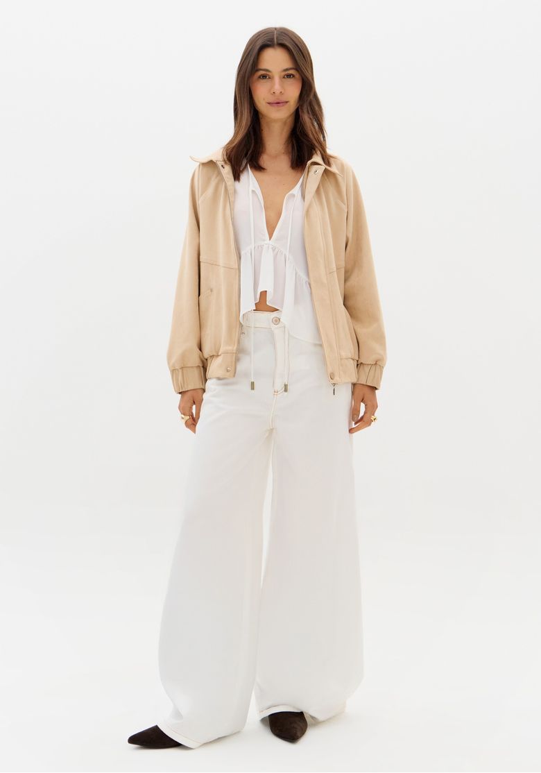Modelo vestindo calça palazzo branca com jaqueta bege e blusa branca.