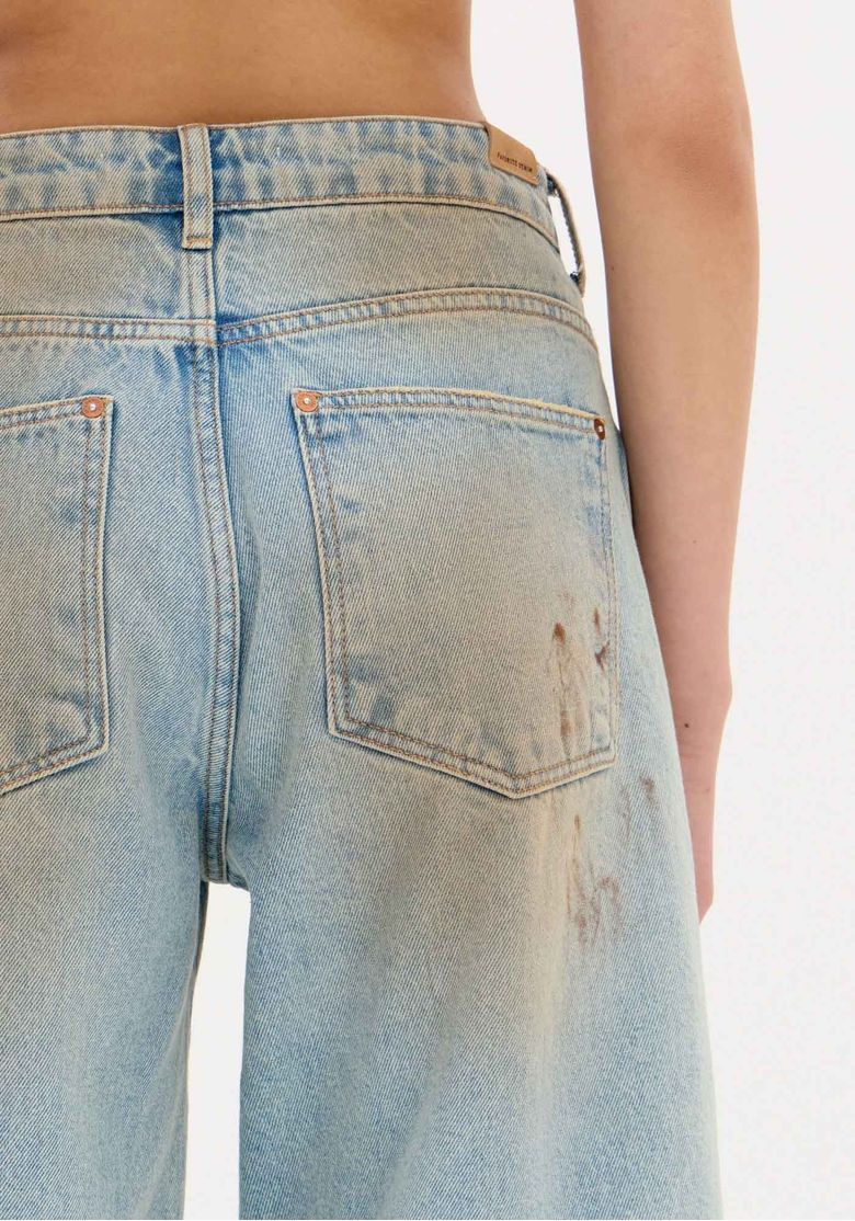 Close frontal da bermuda jeans mostrando cós com passantes, botão metálico e lavagem estonada no denim