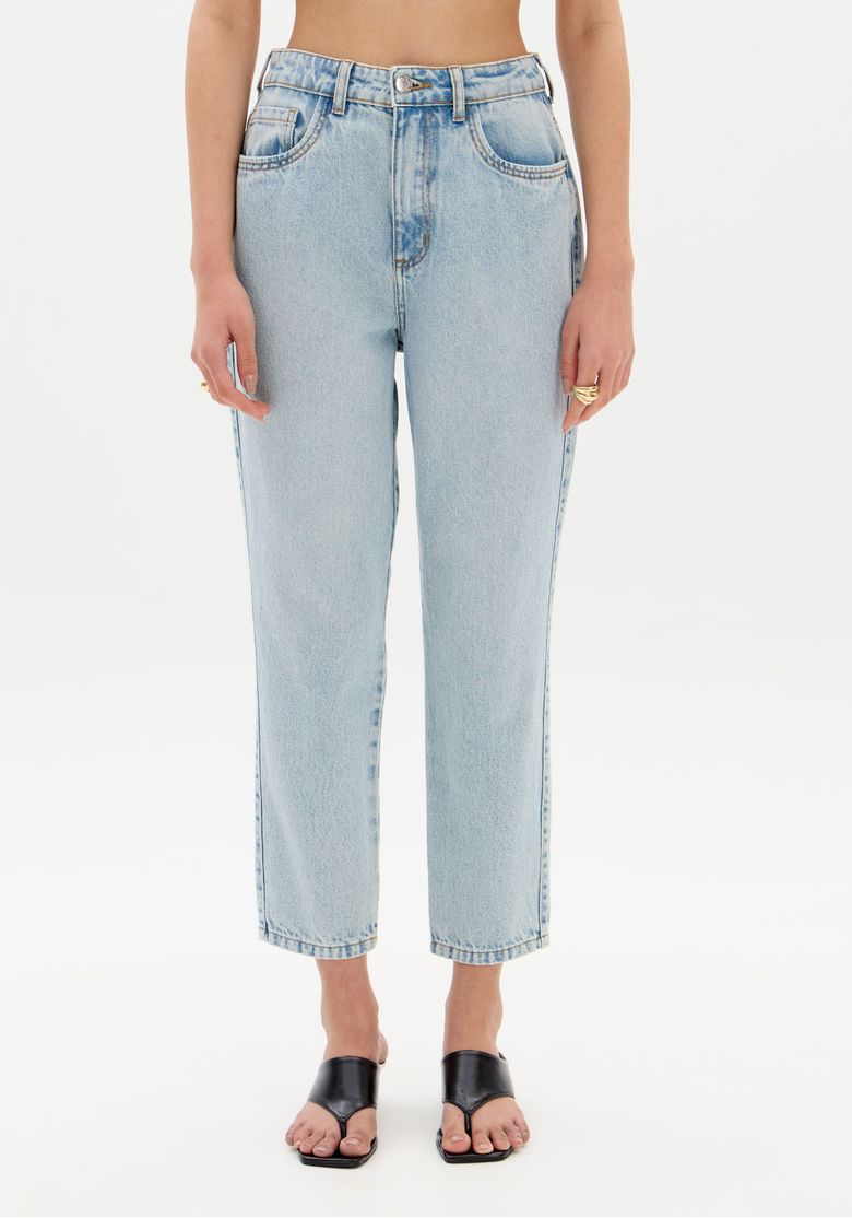 Close frontal da calça mom jeans mostrando cós com passantes, bolsos frontais e lavagem clara em denim