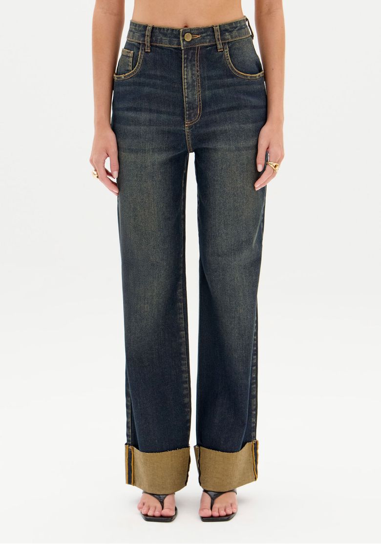 Calça jeans feminina full length lavagem escura vista frontal curta mostrando cintura média, fecho por zíper e barra virada ampla