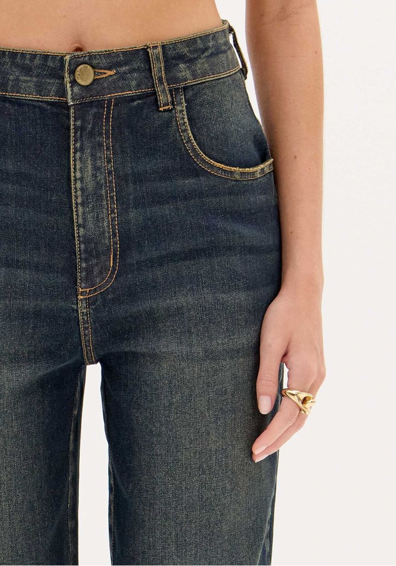 Close-up frontal da calça jeans: detalhe do bolso frontal, costura contrastante e fechamento com zíper e botão