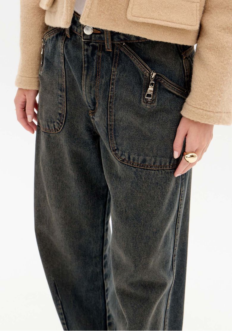 Close frontal da calça baggy destacando costura contrastante, bolsos amplos com zíper e estilo utilitário.