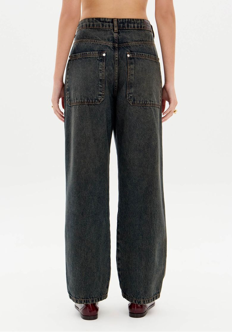 Detalhe lateral da calça com modelagem baggy mostrando bolso inclinado com zíper e tecido denim de alta qualidade.
