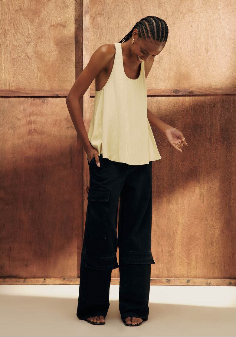 Modelo com regata bege usando calça jeans preta full length cintura média, caimento amplo e recortes marcantes