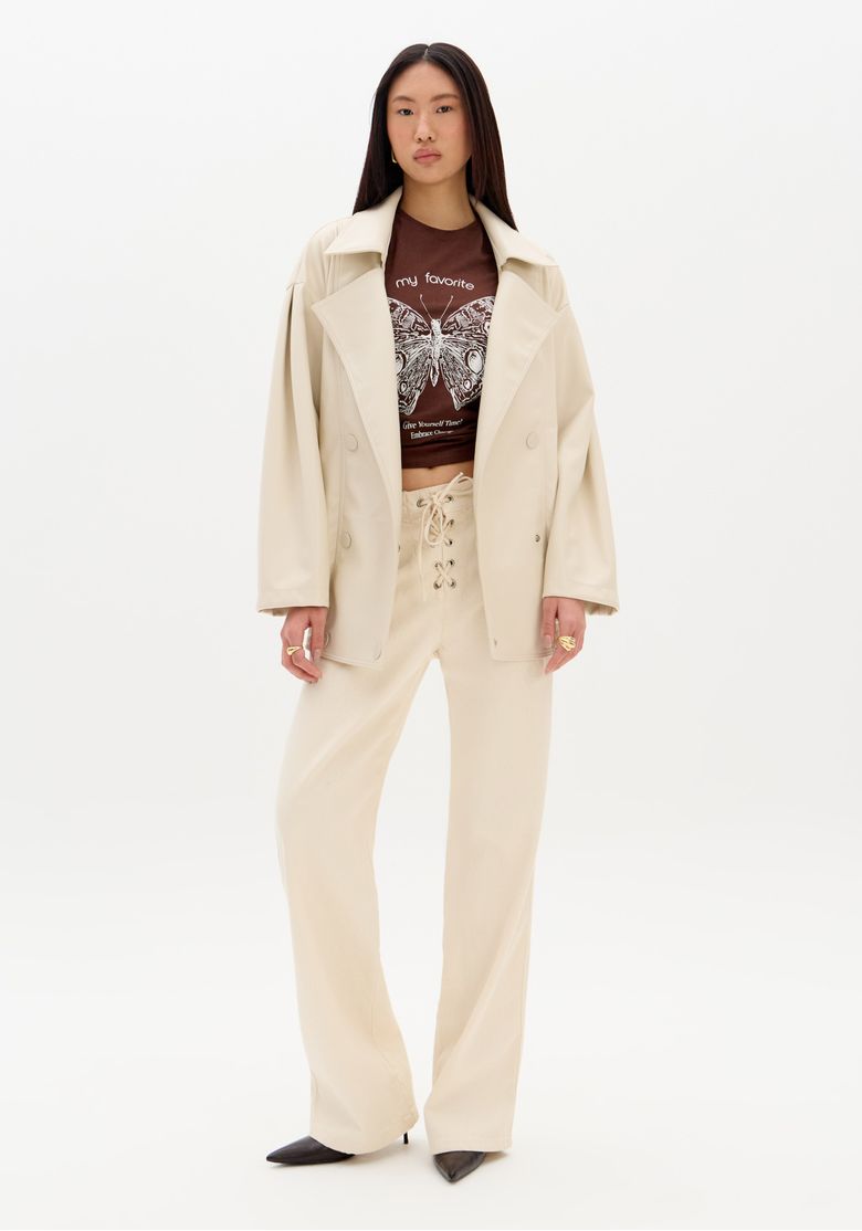 Modelo em pé usando blazer off-white e calça sarja reta branca com amarração frontal no cós, look completo de corpo inteiro