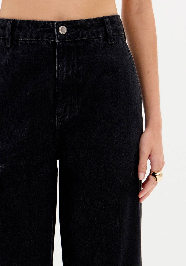 Close-up do cós frontal da calça jeans preta com passantes e fechamento por botão