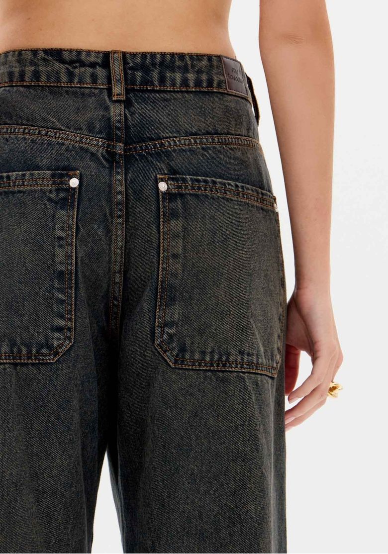 Close nos bolsos traseiros e cós da calça modelo baggy feita com tecido denim 100% algodão e lavagem escura.