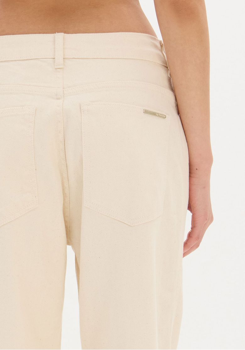 Close-up do bolso traseiro da calça sarja branca com detalhe de costura e etiqueta metálica discreta