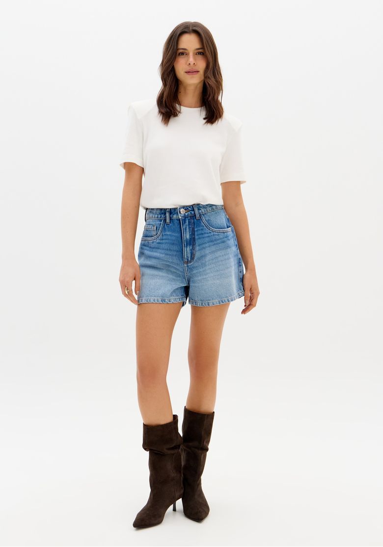 Modelo vestindo short jeans mom azul com cintura alta e botas marrons.