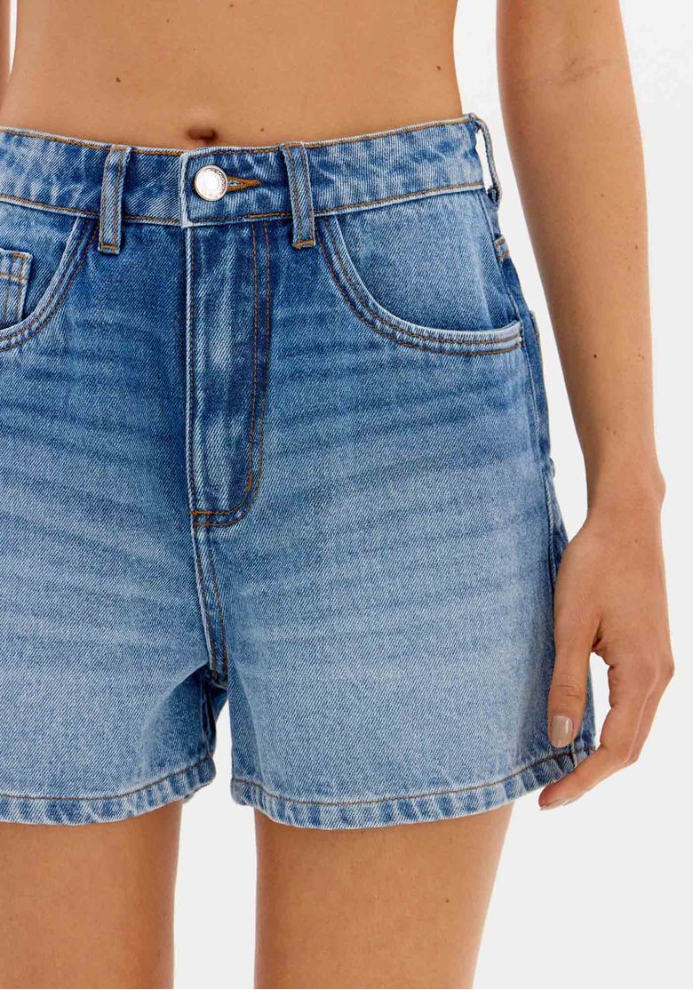 Detalhe frontal do short jeans mom azul, mostrando o fechamento por botão e zíper.