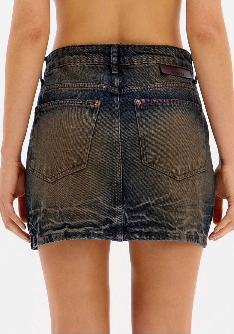 Detalhe lateral da saia jeans curta com lavagem estonada.