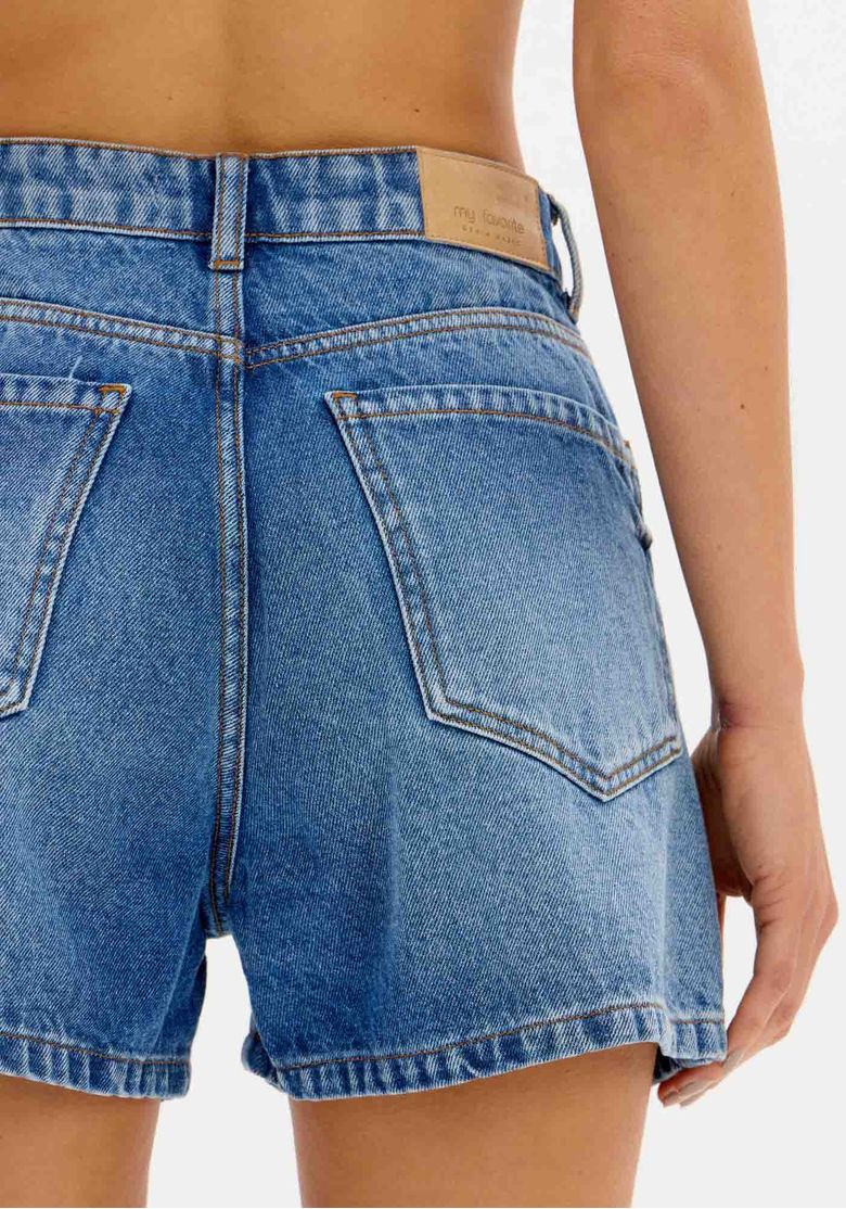Close-up do cós do short jeans mom azul, com passantes para cinto.