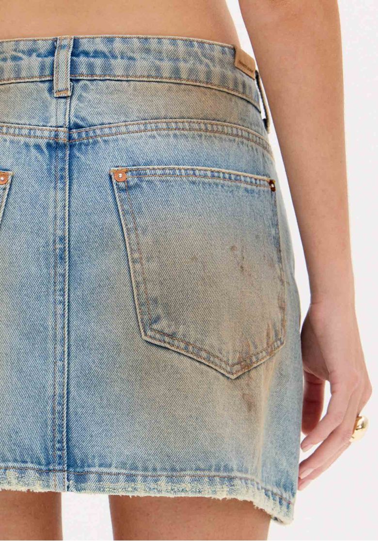 Vista traseira da modelo com saia jeans curta mostrando bolsos posteriores, caimento e barra desfiada.