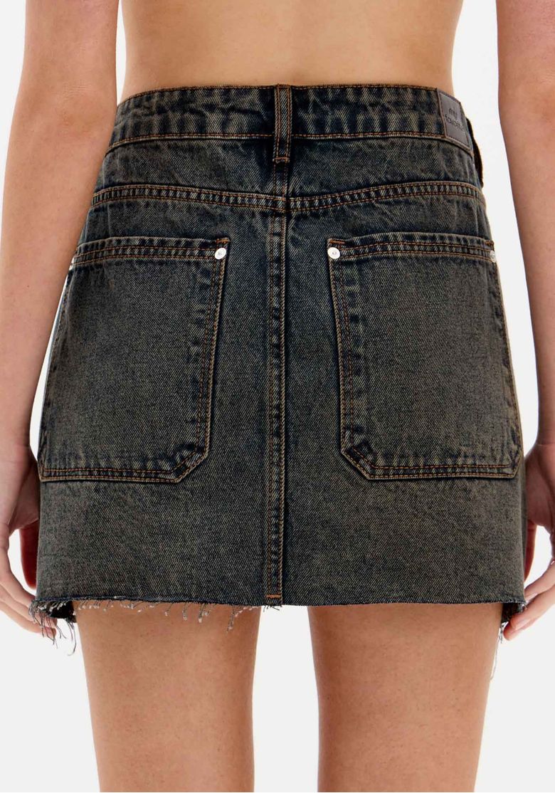 Close-up do cós e bolsos frontais da saia jeans curta, destacando passantes, botão e bolso com detalhe em zíper decorativo.