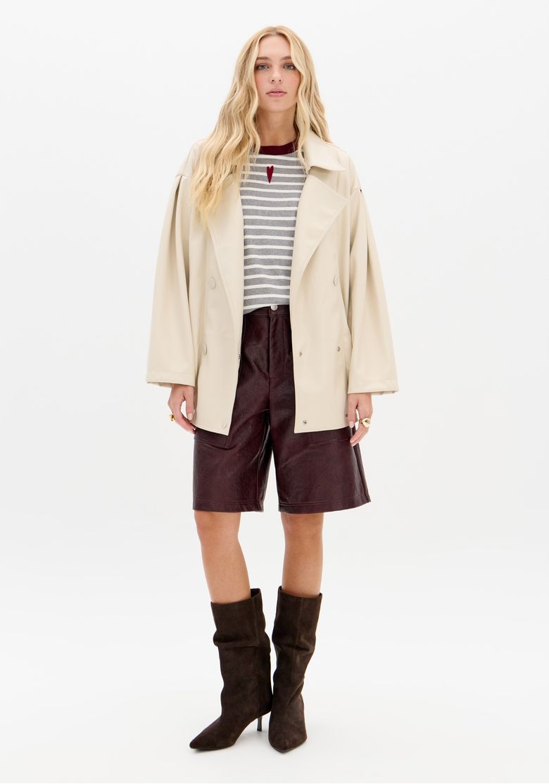 Modelo vestindo bermuda utilitária vinho em PU com jaqueta bege e botas, look urbano com cintura média e bolsos utilitários