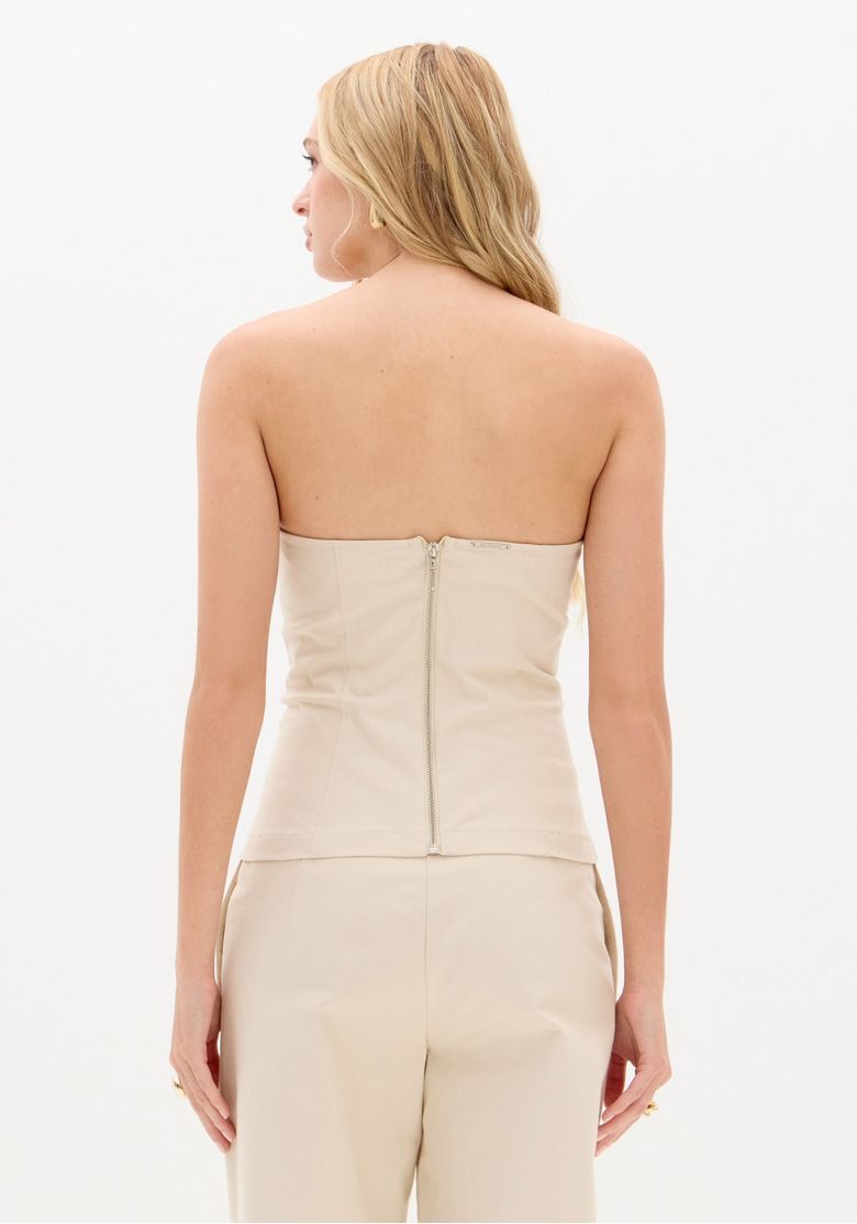 Imagem corpo inteiro com blusa corset sem alças bege combinada com calça bege de perna reta e sapato de bico fino, look minimalista e sofisticado para trabalho