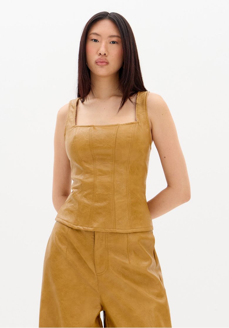 Modelo frontal usando blusa corset de alça em PU bege com recortes estruturados e caimento ajustado