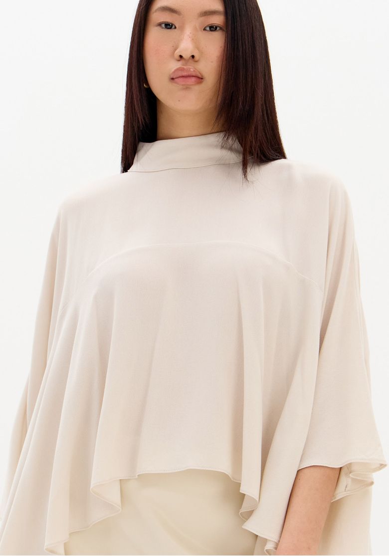 Look completo frontal com blusa bata bege e saia mini bege, babados que criam movimento e silhueta ampla