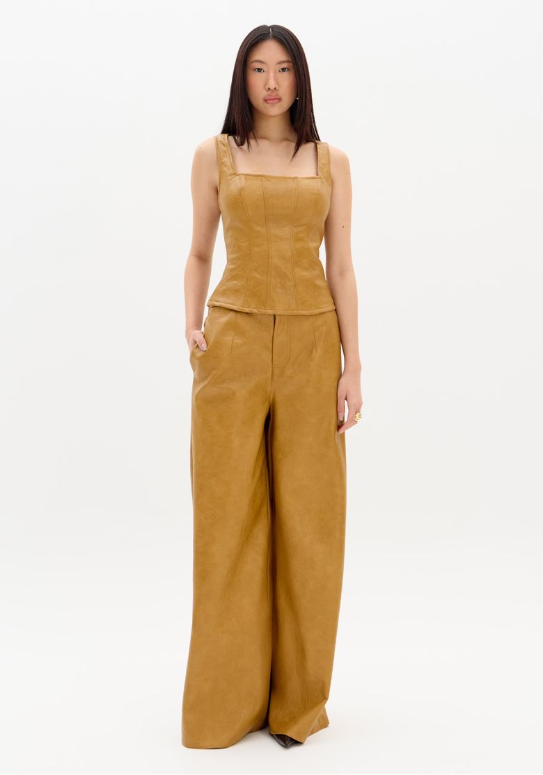 Visão full body da modelo com blusa corset e calça pantalona em PU bege, look coordenado e silhueta alongada