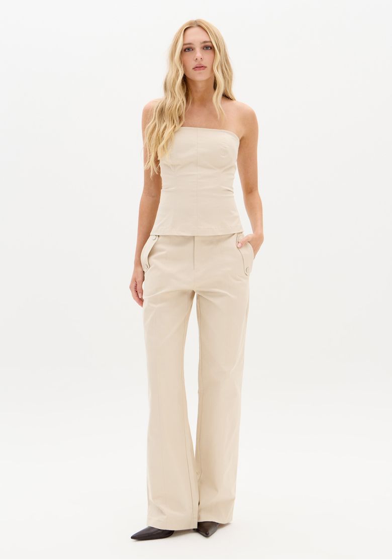 Frente da modelo usando blusa corset sem alças bege, caimento justo até a barra reta na altura do quadril, visual minimalista combinado com calça bege