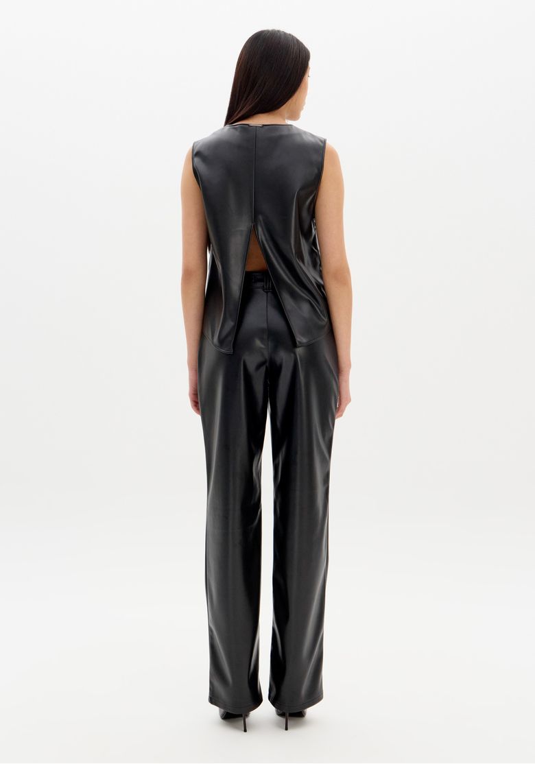 Visão full body traseira: blusa preta com abertura nas costas e painéis sobrepostos, acompanhada de calça reta e salto
