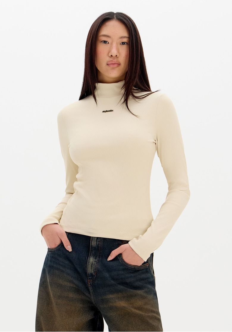 Blusa feminina gola alta canelada bege vista frontal corpo inteiro, manga longa e caimento justo em malha pesada, modelo combinando com calça jeans