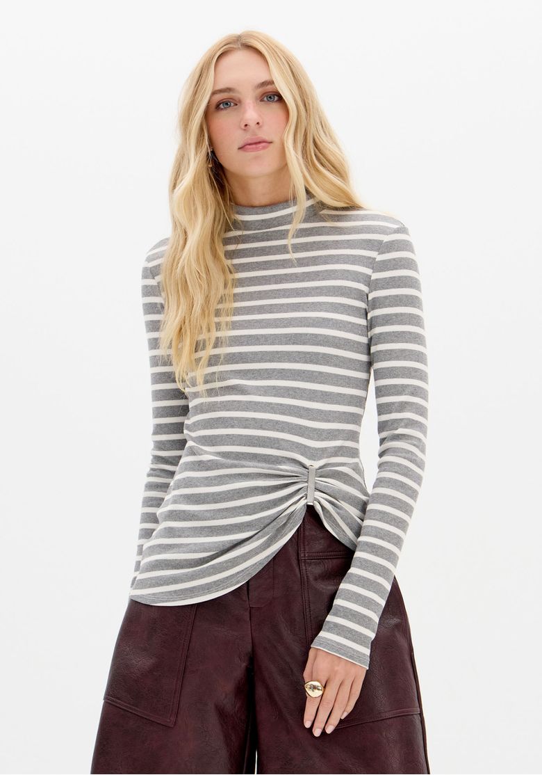 Modelo frontal usando blusa listrada gola alta manga longa com detalhe torcido na barra, vista frontal em estúdio